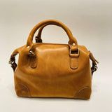 Vintage tan leather Boston bag with dual top handles and brass hardware on a plain background