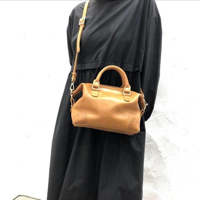 Handcrafted tan leather Boston bag with top handles and crossbody strap, worn over black dress
