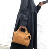Woman in black dress holding tan vintage leather Boston bag with top handles