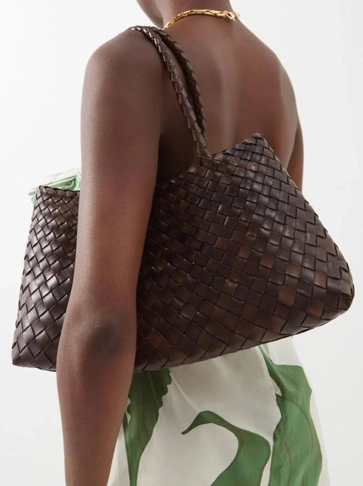 Woman wearing a brown woven leather hobo bag with trapezoidal shape on shoulder