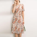 Woman wearing a light pink floral embroidered silk midi dress with short sleeves and waist tie.