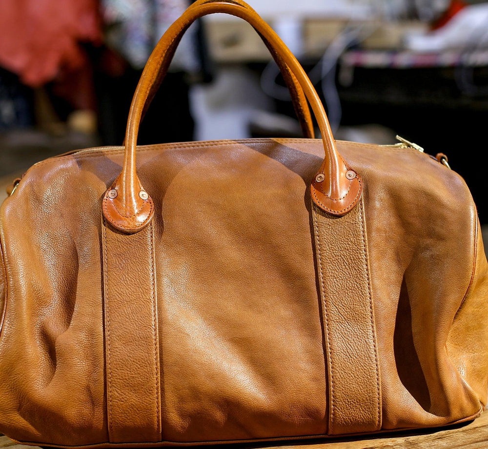 Large brown leather weekend duffle bag with dual handles on a wooden surface, ideal for travel