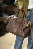 Person holding a large brown leather weekend bag with dual handles and a zipper closure.
