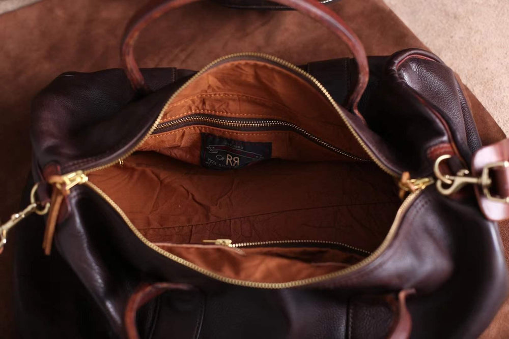 Open view of a black and brown leather weekend bag with gold zipper and spacious tan interior.