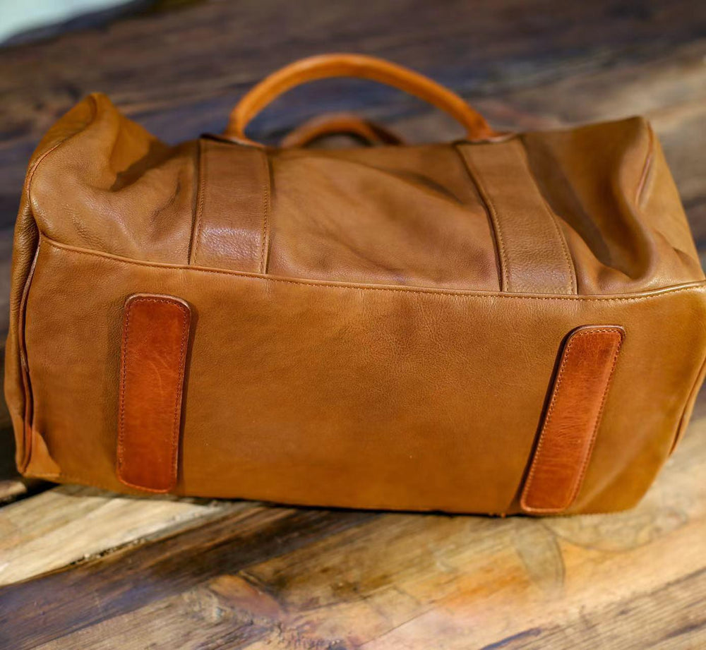Brown genuine leather duffle bag with reinforced base, placed on rustic wood surface