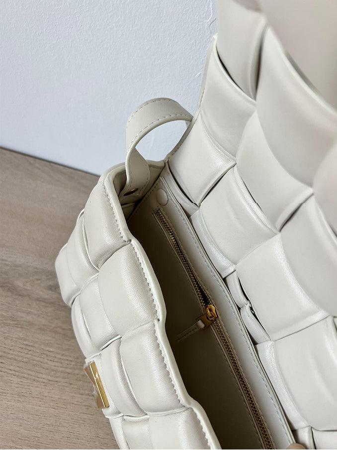 Close-up of white woven leather handbag with gold zipper and textured design on wood surface