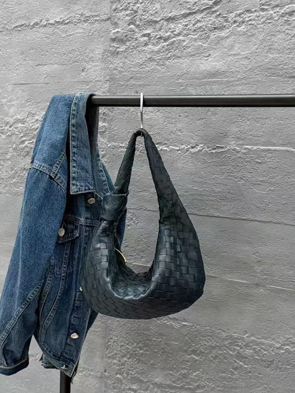 Black woven leather hobo bag and denim jacket on a metal rack against a concrete wall