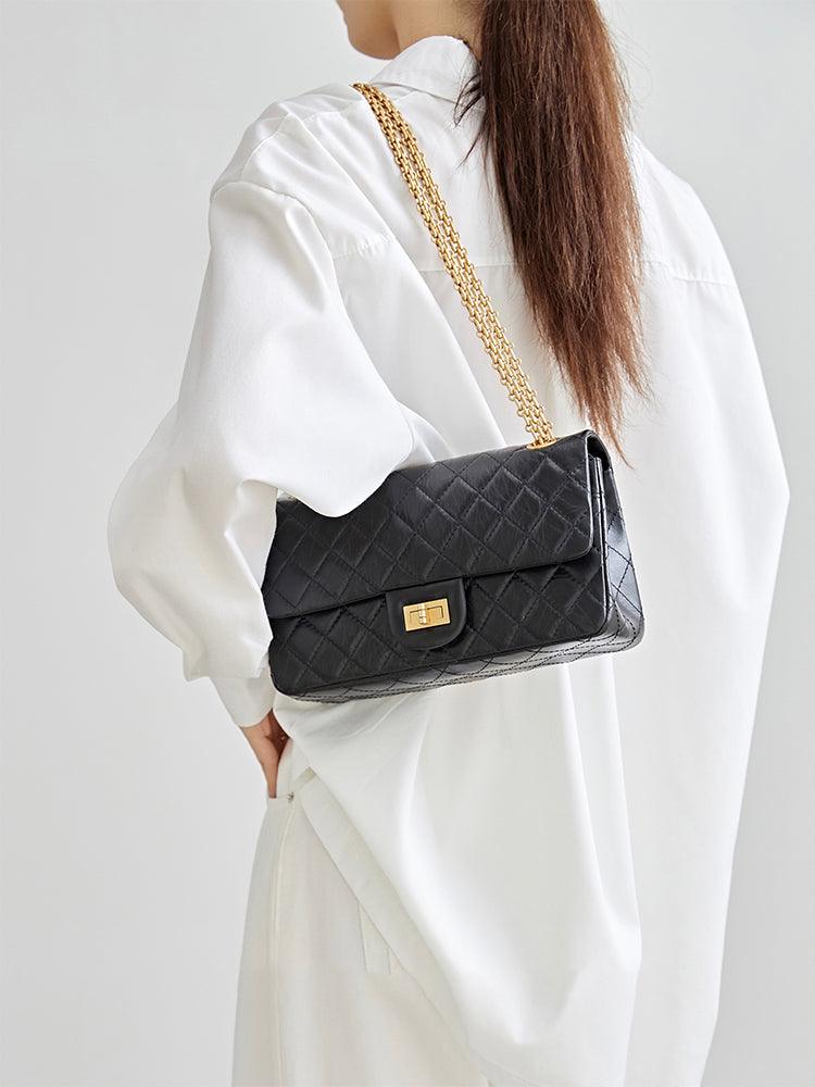 Woman in white shirt carrying black quilted leather shoulder bag with gold chain strap