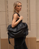 Woman carrying a large black grain leather shoulder bag with zipper, stylish travel crossbody