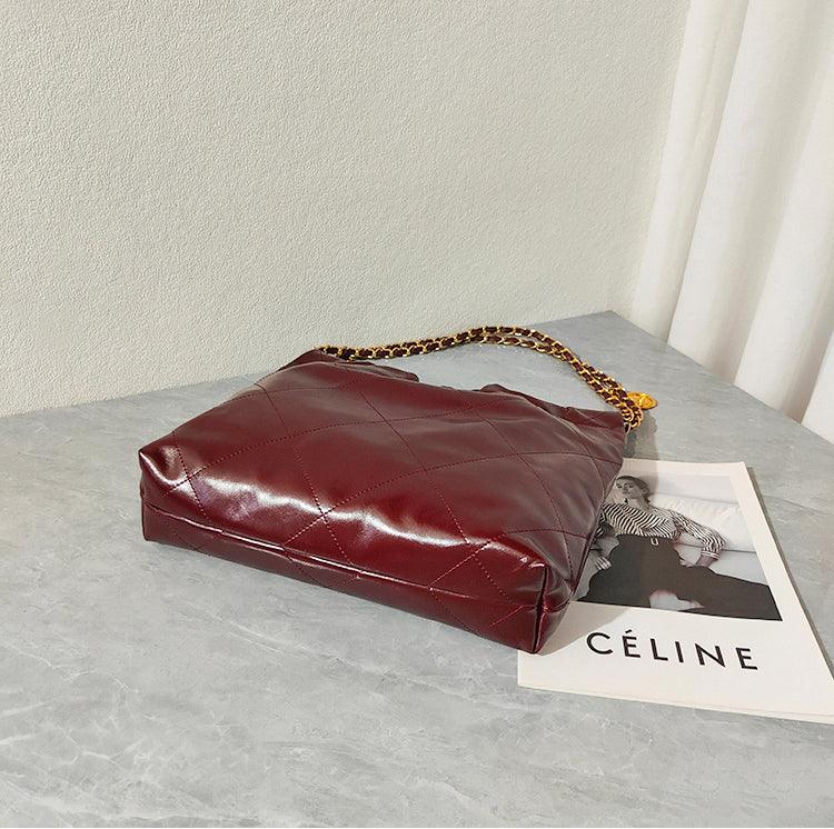 Large quilted calfskin leather shoulder bag in burgundy with gold-tone chain strap on a marble table