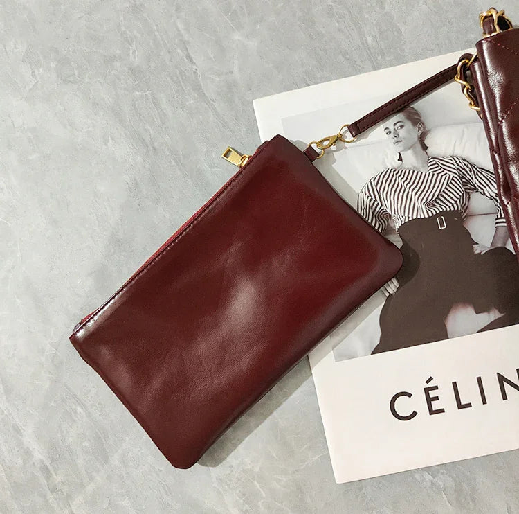 Minimalist burgundy leather pouch bag with gold hardware on a marble surface