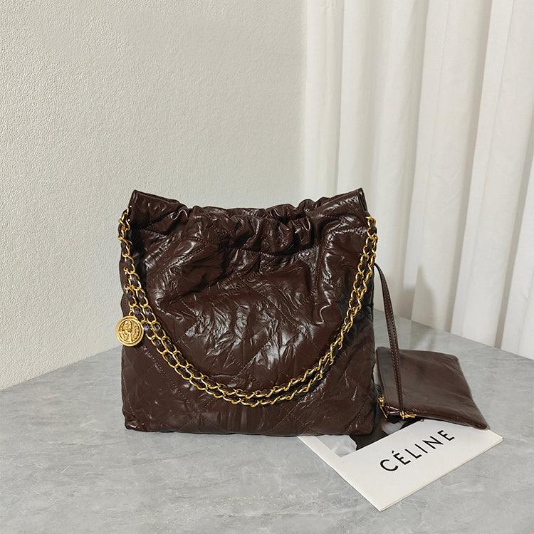 Large brown calfskin leather shoulder bag with gold chain strap on a grey surface
