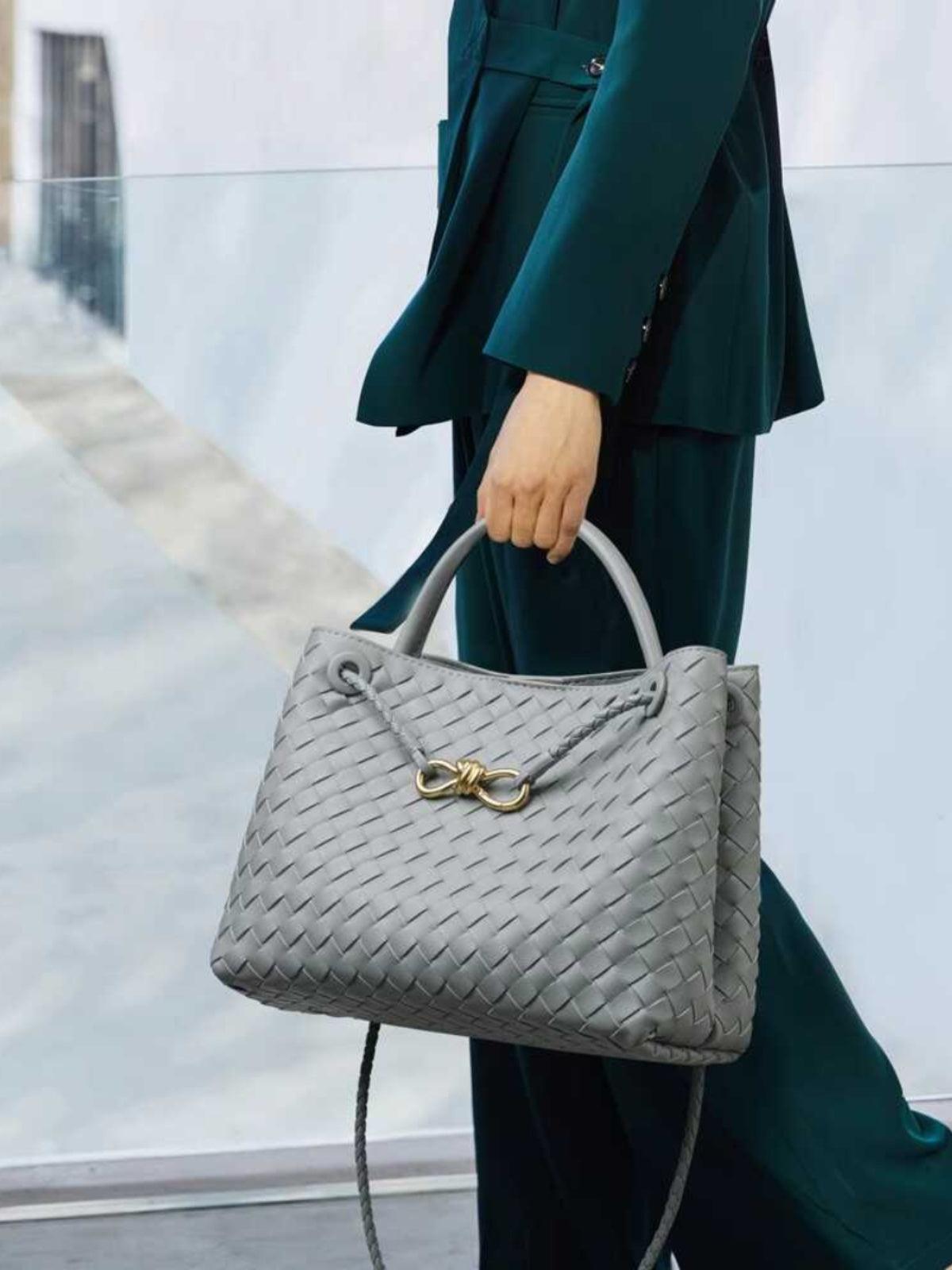Grey woven leather shoulder bag with gold metal buckle, held by person in dark green suit
