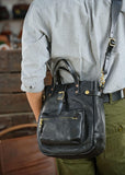Handmade black cowhide leather crossbody shoulder bag with gold hardware, worn by person