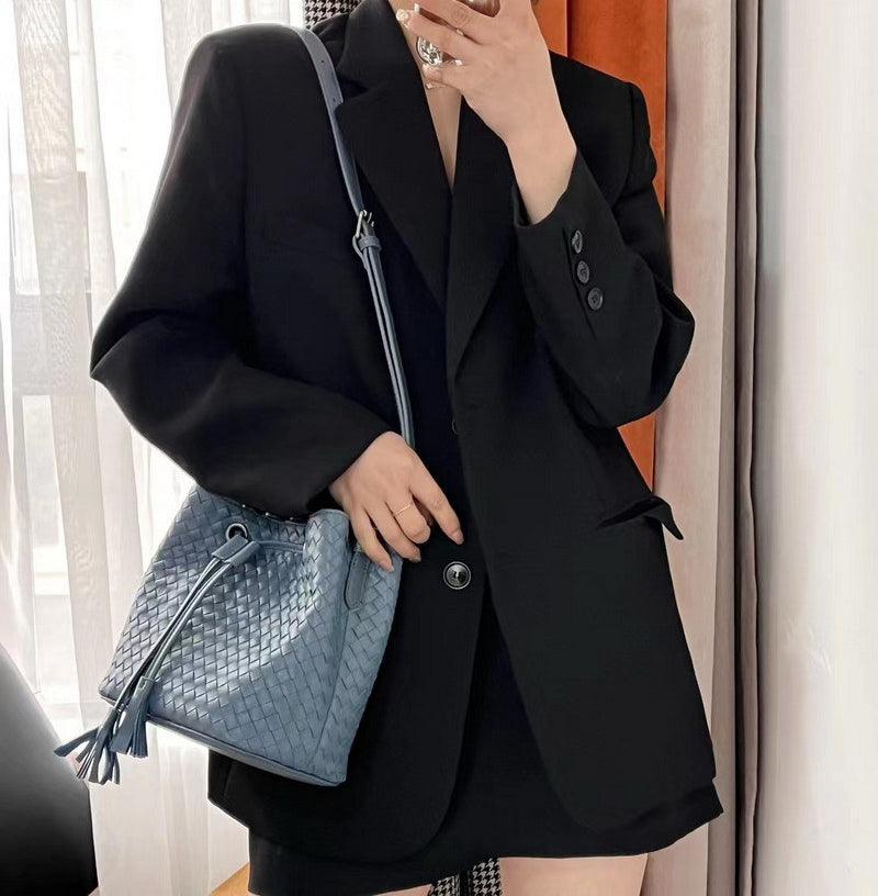 Woman in black blazer holding medium blue handwoven lambskin leather drawstring bucket bag