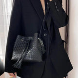 Handwoven black lambskin leather bucket bag with drawstring, crossbody style, worn by a woman in a black blazer