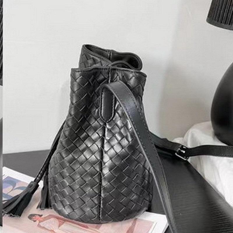 Black handwoven lambskin leather bucket bag with drawstring and shoulder strap on table