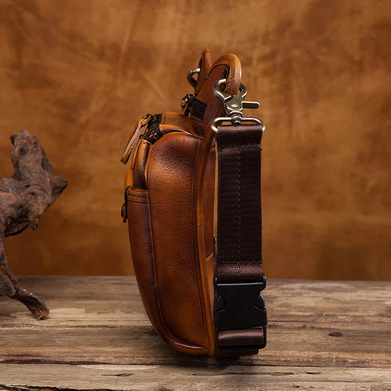 Full grain brown leather leg bag with brass hardware and adjustable strap on rustic wood table