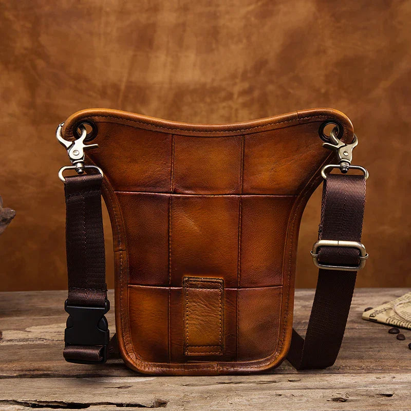 Full grain leather leg bag with stitched details and adjustable brown straps on rustic wood table