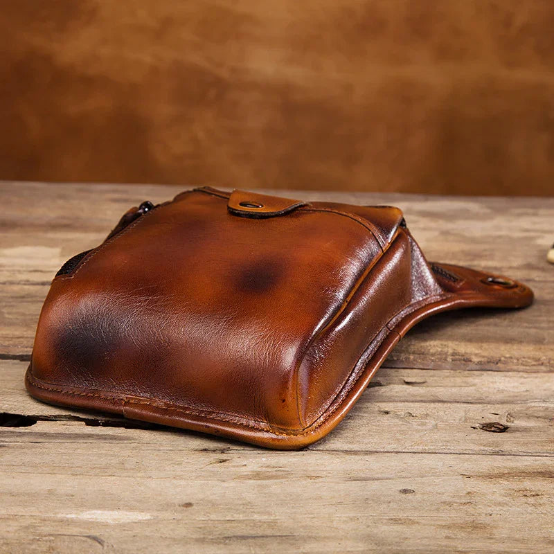 Full grain brown leather leg bag with snap closure on rustic wooden surface
