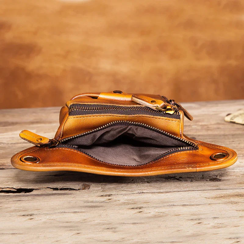 Open brown full grain leather waist bag with zippers, displayed on rustic wooden surface
