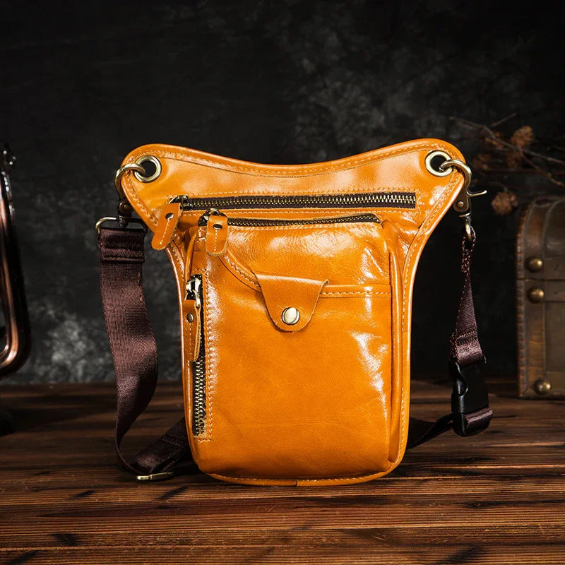 Full grain tan leather leg bag with multiple zip pockets and black adjustable strap on wood table