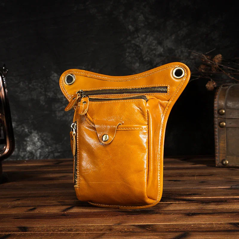 Full grain leather leg bag in tan with multiple zippered pockets on a wooden surface