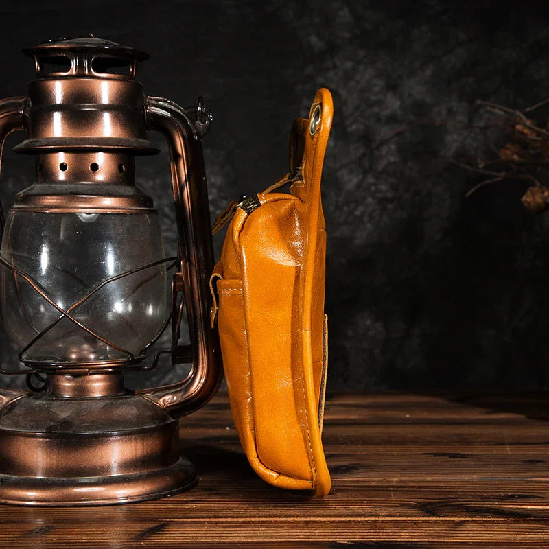 Side view of yellow full grain leather leg bag on wooden table beside vintage lantern
