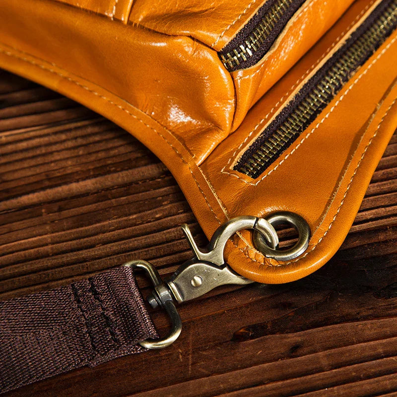 Close-up of full grain leather leg bag with brass hardware and zipper pockets on wood