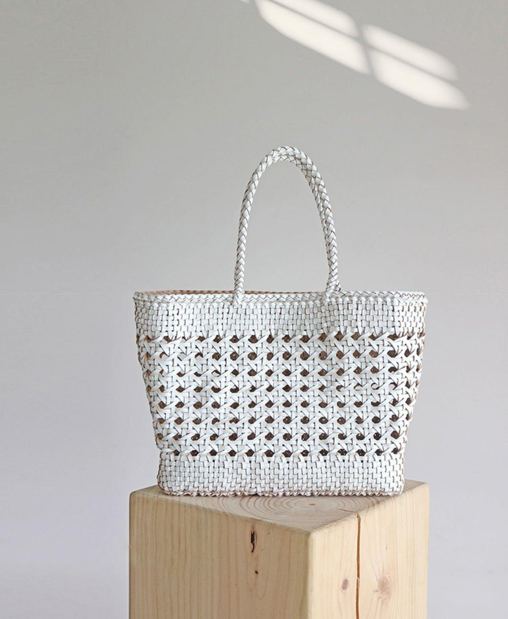 White hand-woven genuine leather tote bag with cuboid shape and braided handles on wood block