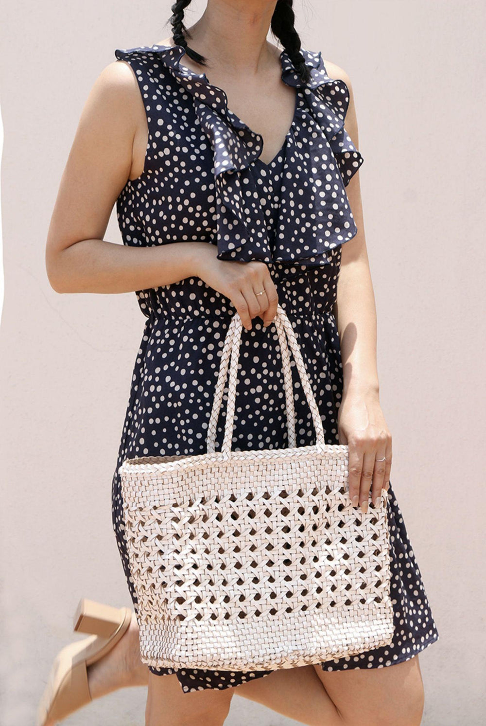 Woman in polka dot dress holding a hand-woven leather rattan tote bag with double handles