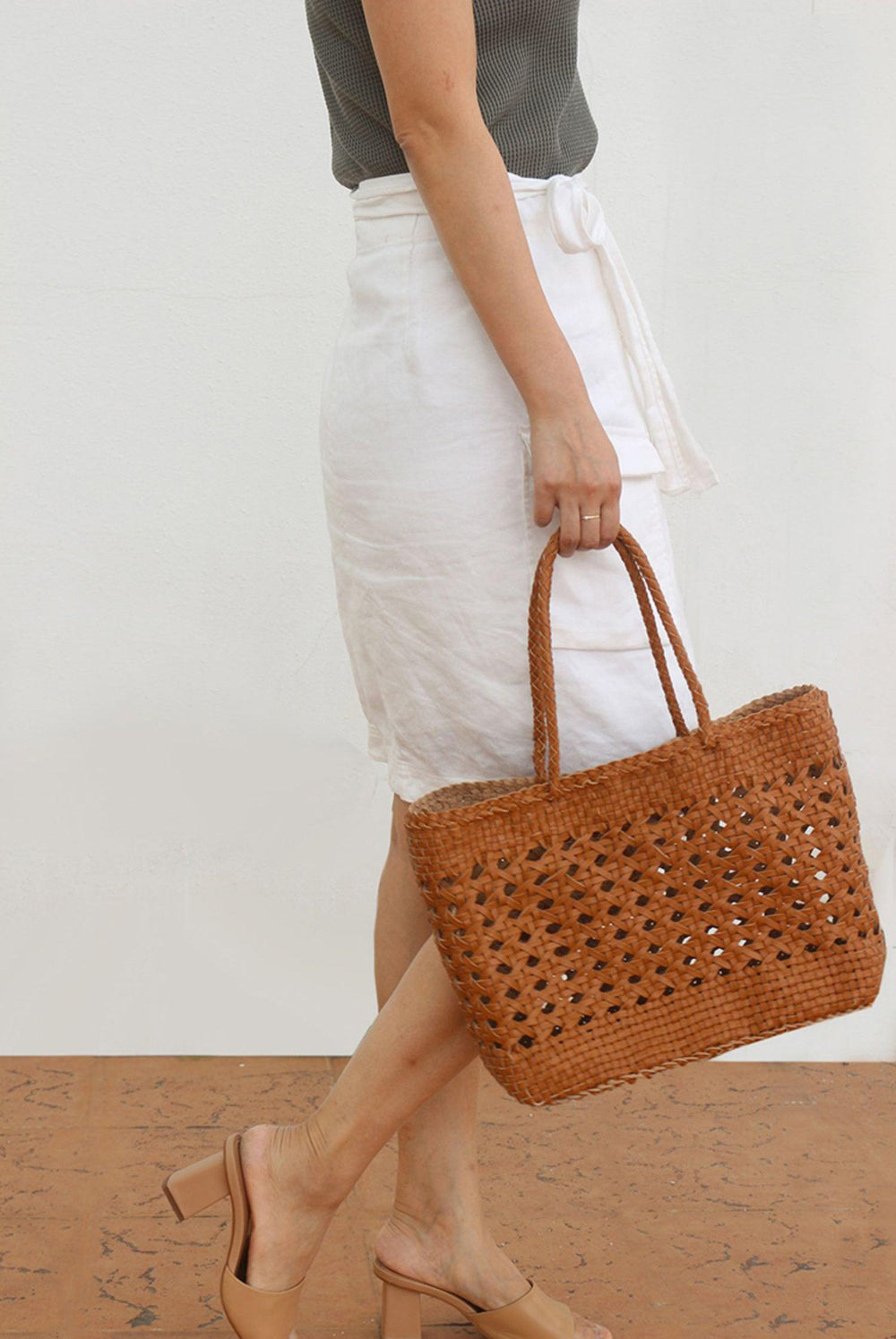 Woman holding a hand-woven leather tote bag with rattan pattern, styled for summer or holiday