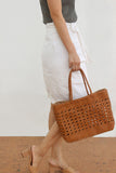 Woman holding a hand-woven leather tote bag with rattan pattern, styled for summer or holiday