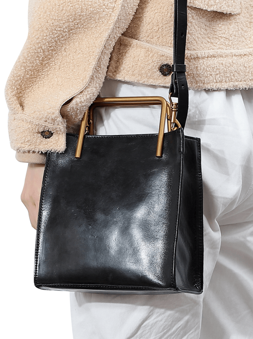 Woman carrying a black genuine cowhide leather shoulder bag with gold metal handle