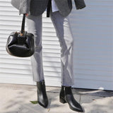 Woman holding black genuine leather round handbag with gold lock, wearing grey pants and black boots
