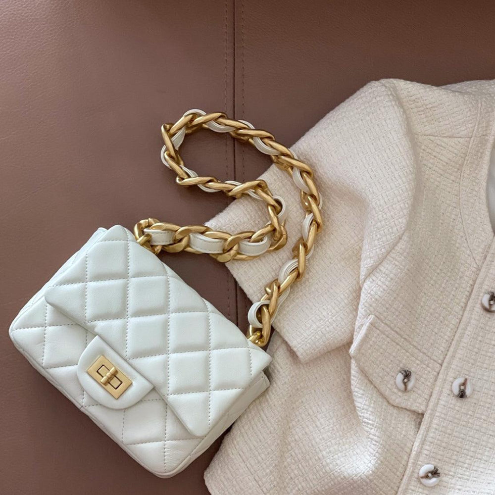 White quilted leather shoulder bag with gold chain strap and turn-lock, styled on a cream jacket.