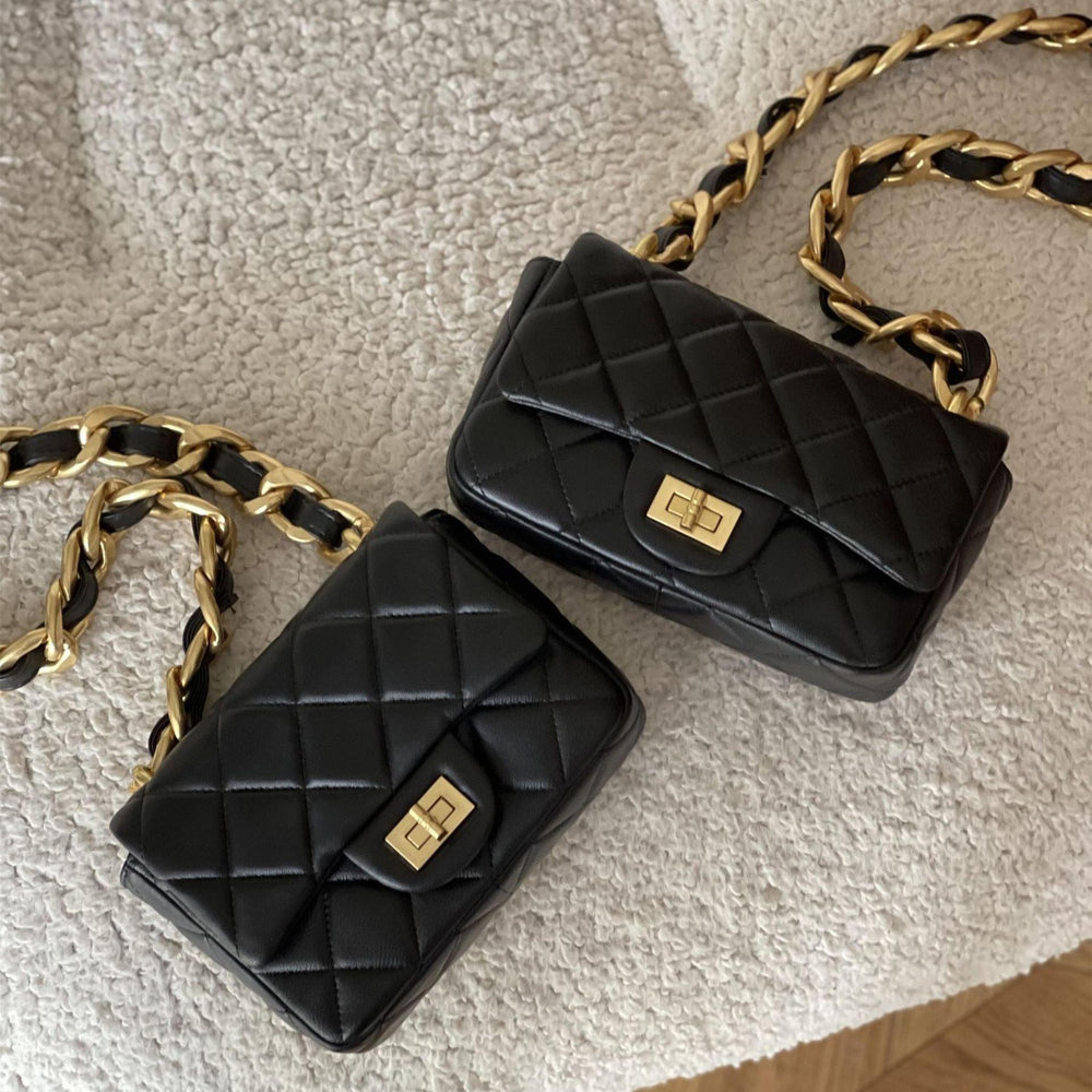 Two black quilted leather shoulder bags with gold chain straps and gold turn-lock closures on a textured surface