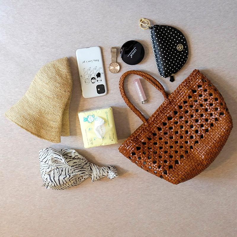 Genuine leather handwoven tote bag with open rattan weave, surrounded by daily essentials.