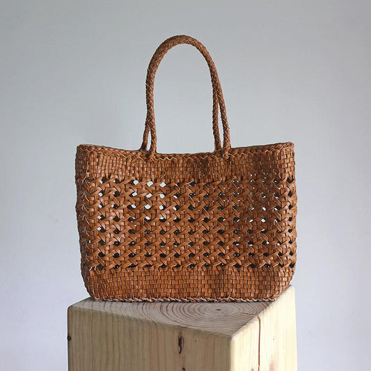 Handwoven brown leather tote bag with cuboid shape and intricate open rattan weave, displayed on a wooden block
