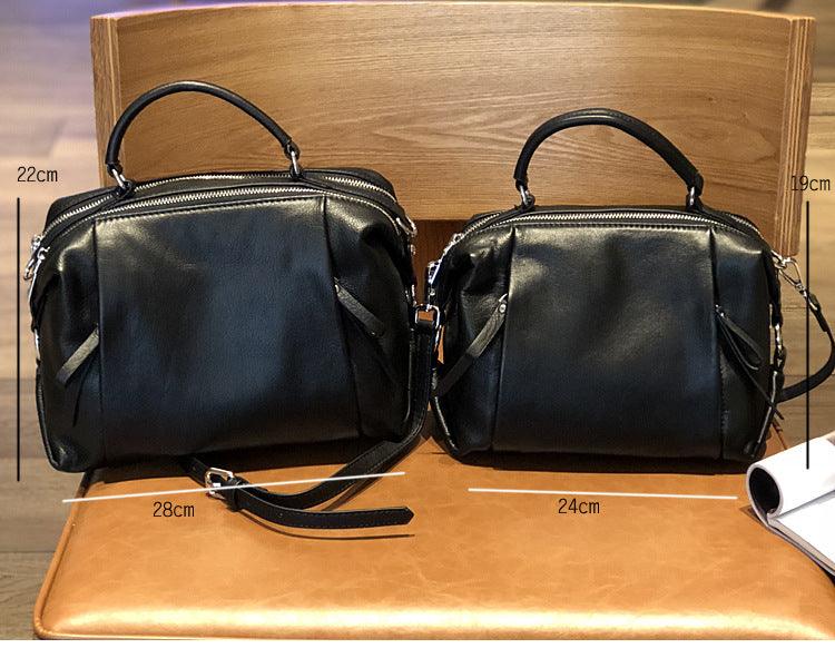 Two black genuine leather handbags in different sizes with top handles and shoulder straps, displayed on a chair with size measurements visible.