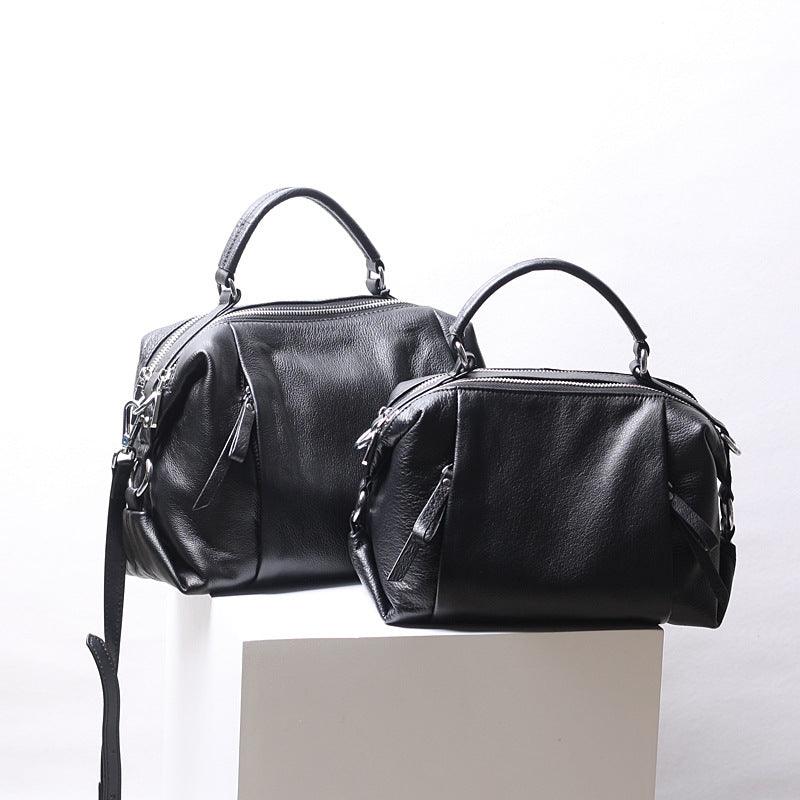 Two black genuine leather Boston handbags with top handles and detachable straps on white display