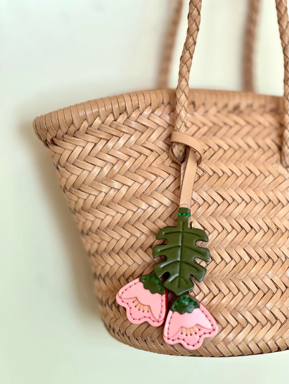 Hand-woven cowhide leather bucket bag with braided straps and pink floral leather charm