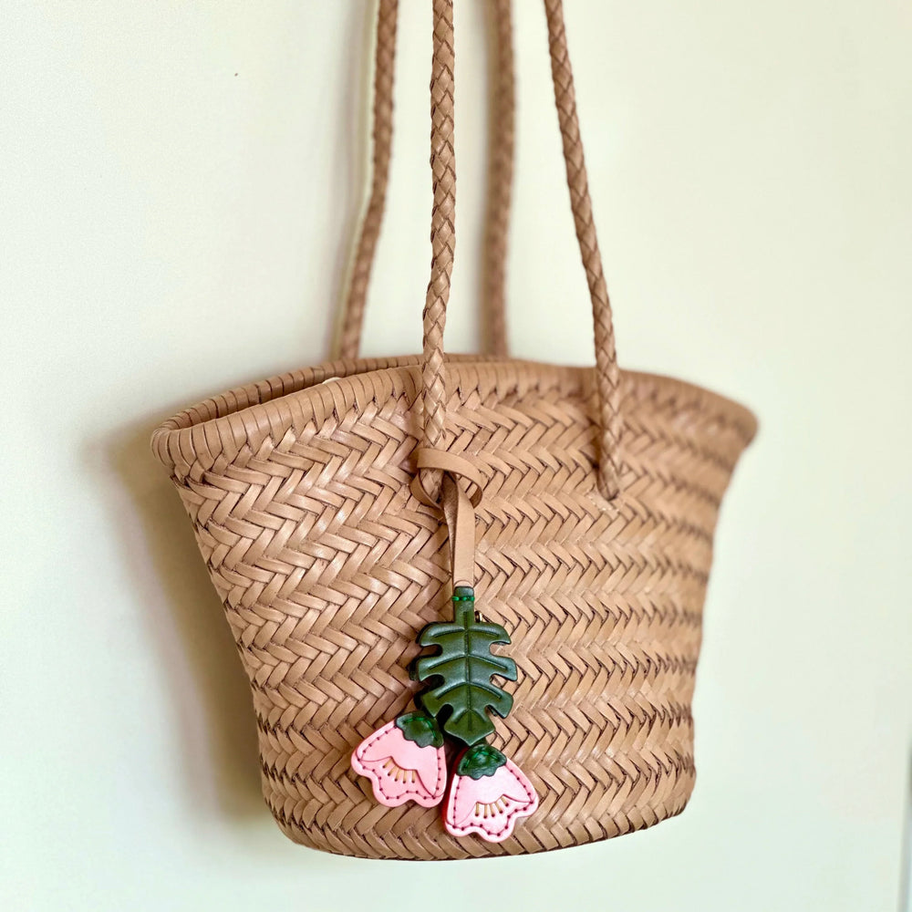 Hand-woven cowhide leather bucket bag with braided straps and pink floral charm