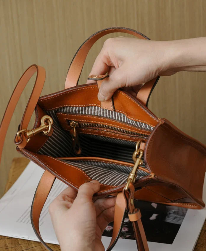Handcrafted brown cowhide leather handbag with striped interior, zip pocket, and gold hardware
