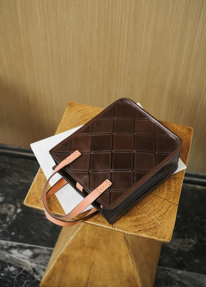 Handcrafted brown cowhide leather handbag with tan handles on a wooden table
