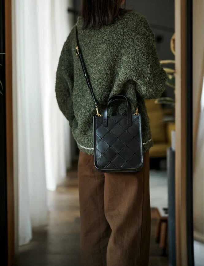 Woman wearing a black quilted leather crossbody bag with top handles indoors