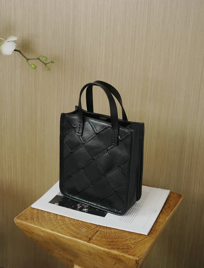 Black cowhide leather handbag with quilted pattern, top handles, on wooden table