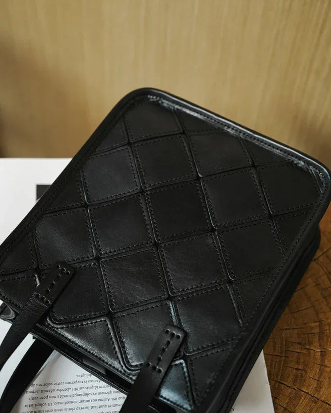 Black cowhide leather handbag with diamond quilted pattern and shoulder straps on wooden surface