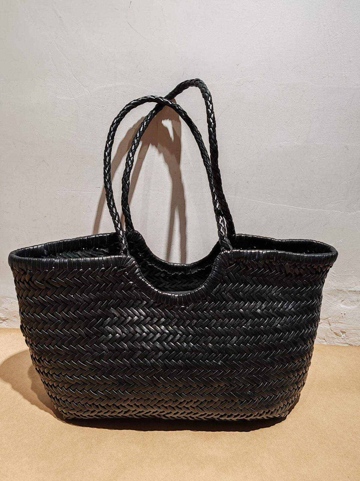 Handcrafted black woven leather tote bag with braided handles on a neutral background