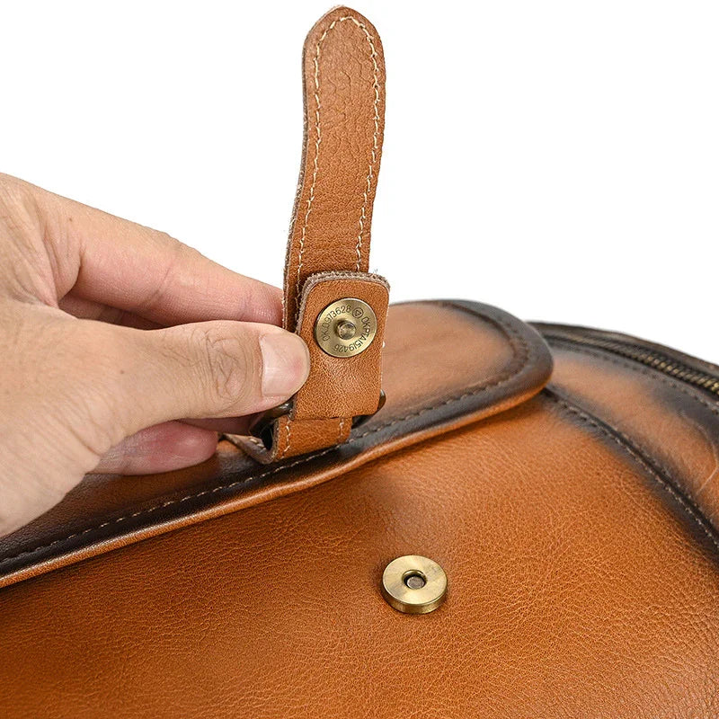 Close-up of a hand fastening a full-grain brown leather duffle bag with a brass snap button